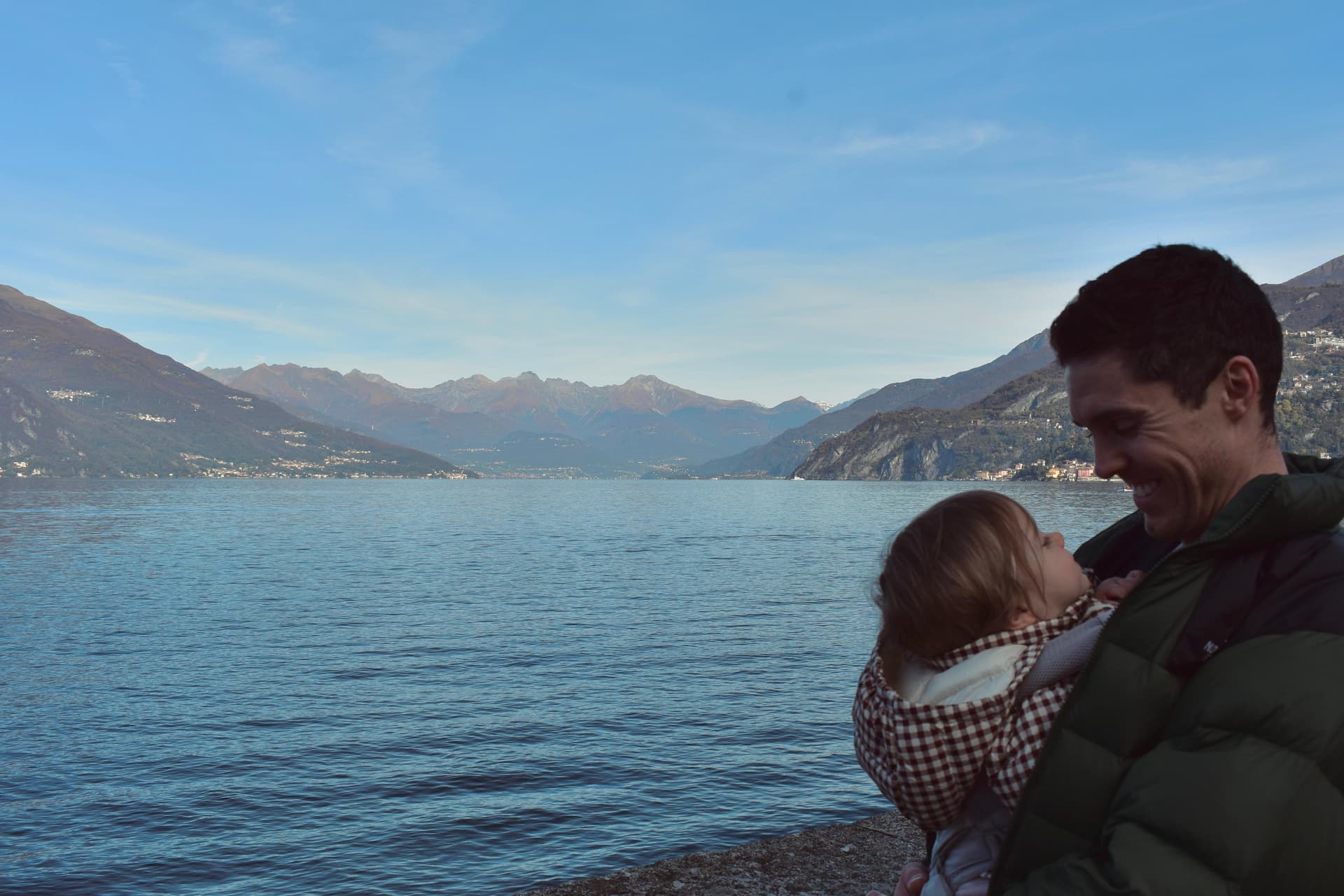 A parent holding their baby, looking out over the water